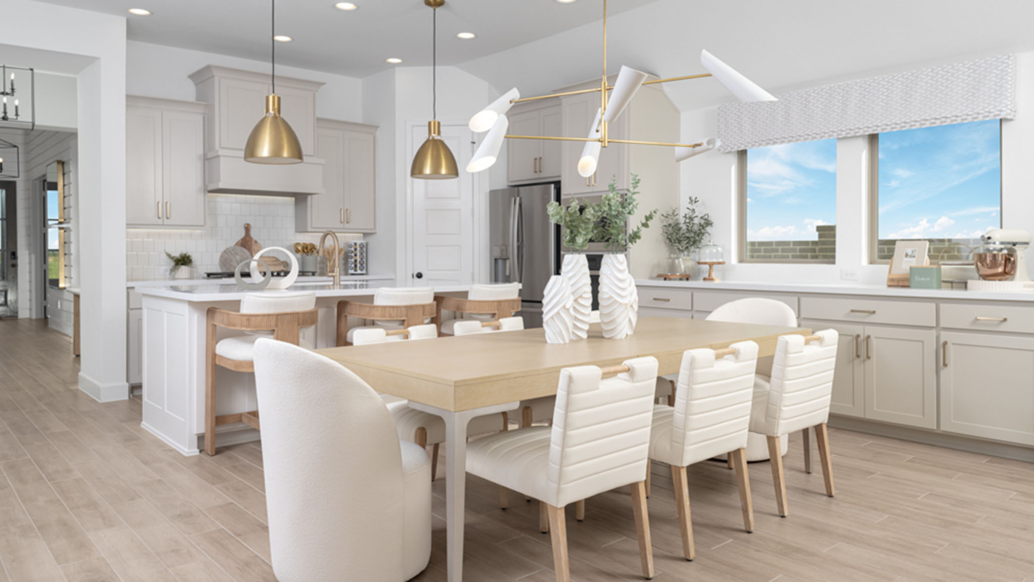 Open-concept kitchen and dining room with white cabinetry, gold pendant lighting, and large dining table seating eight.