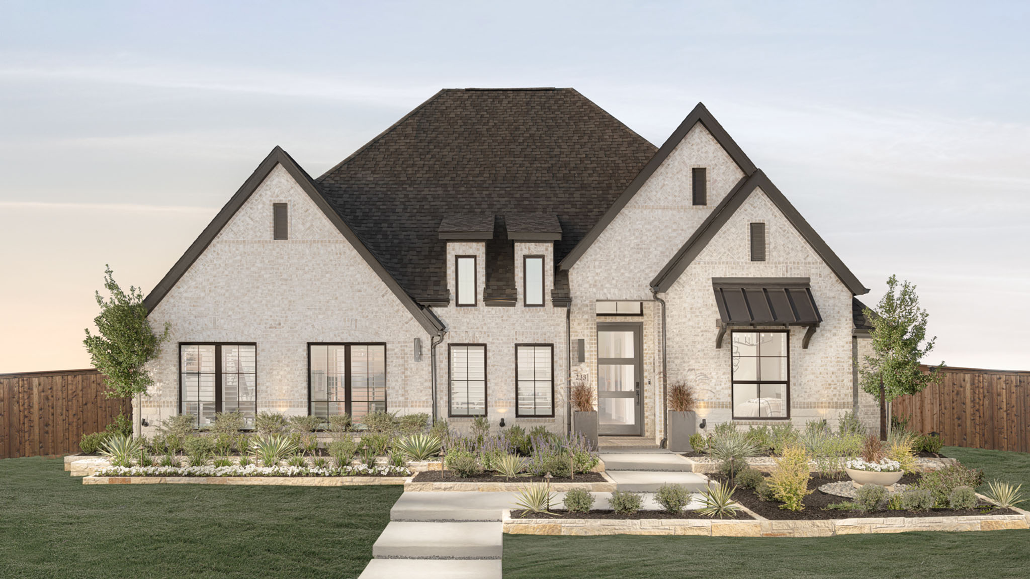 Two-story brick home with steep gabled roofline and landscaped front yard at dusk.